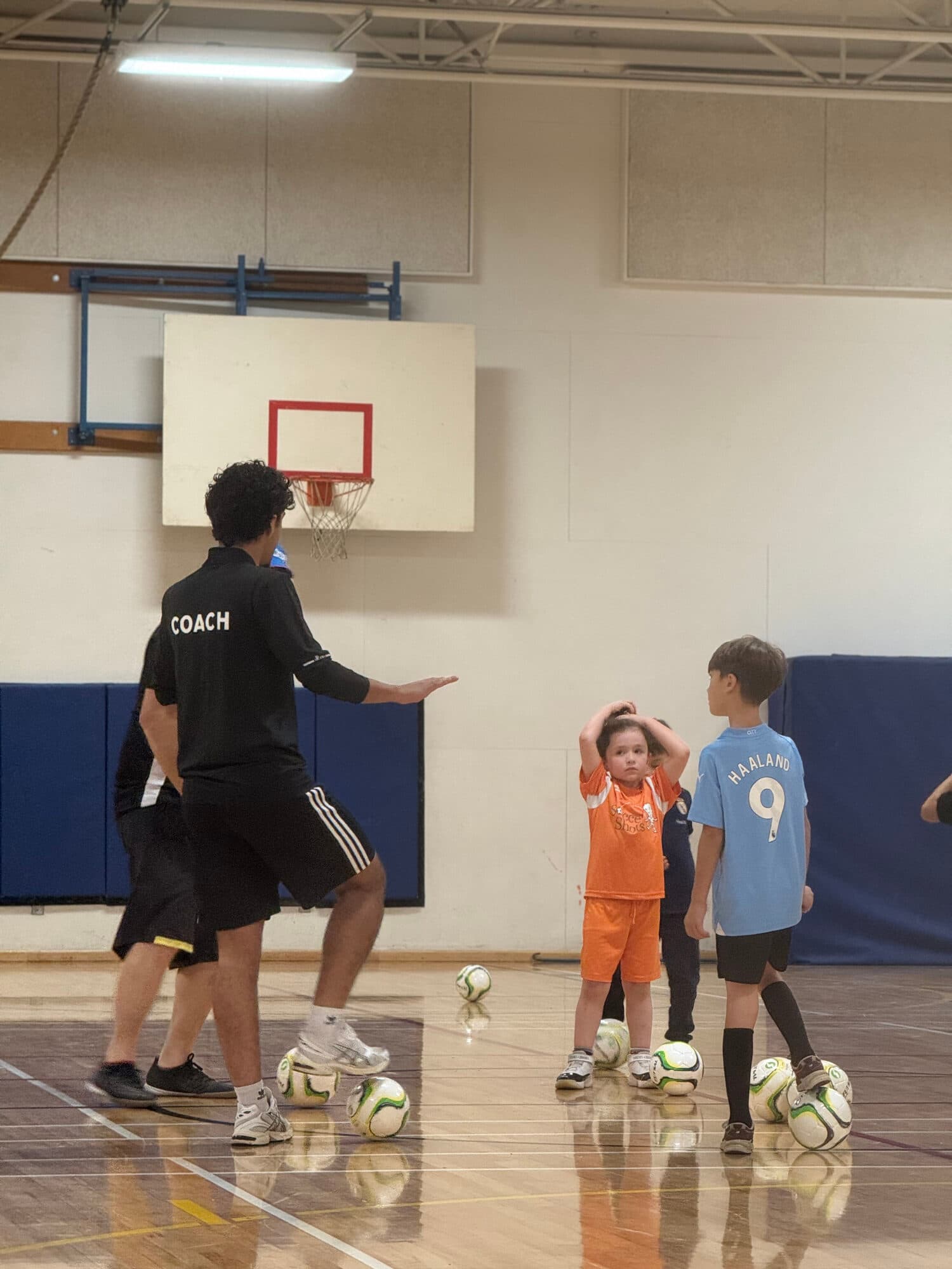 Coach Yusif instructing young players on the court, ball at their feet